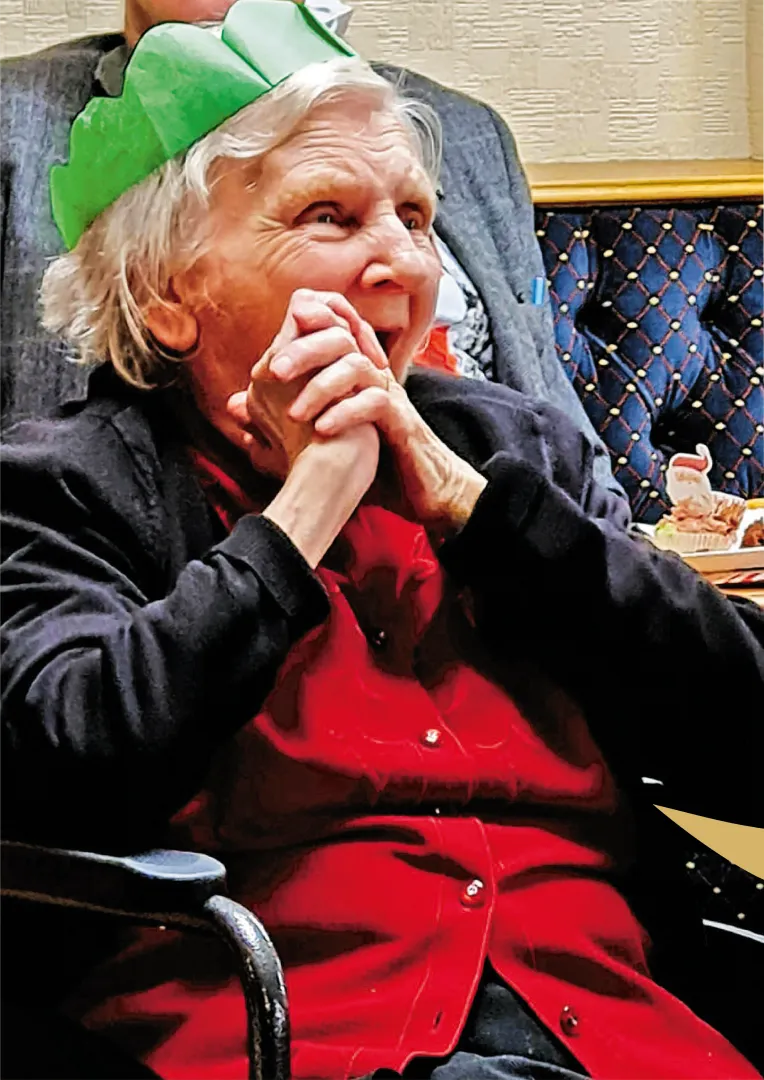 Elderly client smiling brightly and wearing a green party hat during a festive Astar Homecare celebration.