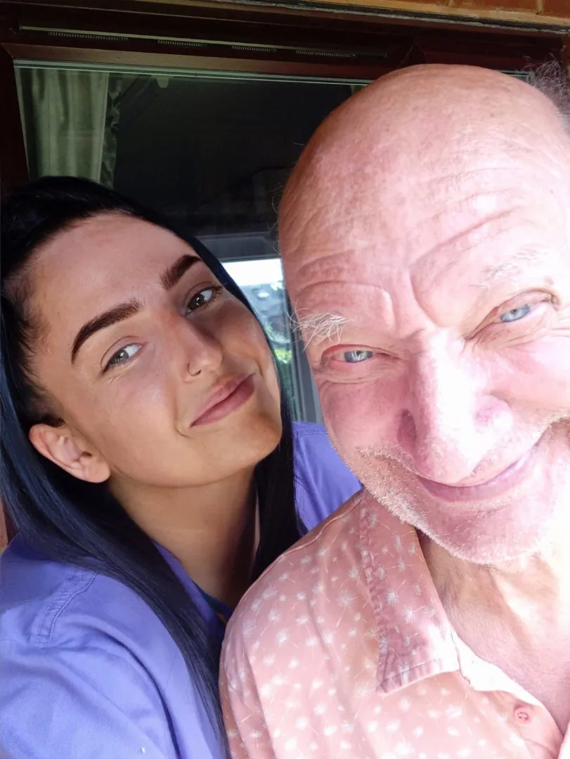 Smiling elderly woman holding a red handled cup, enjoying a warm moment in a cosy Astar Homecare setting.
