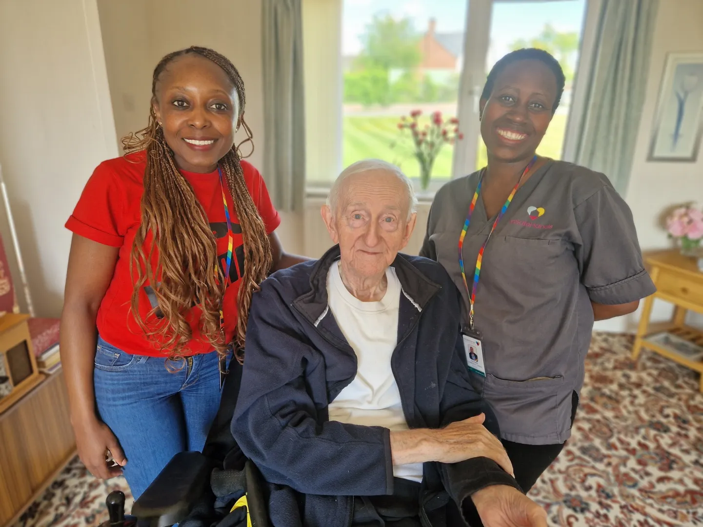 Astar Homecare carers and a female client in a wheelchair enjoying the sunshine outside residential housing.