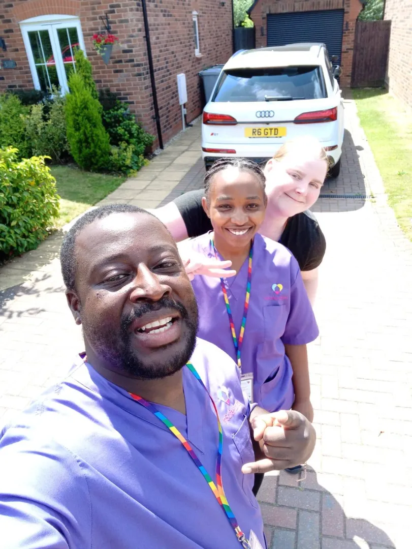 Portrait of an Astar Homecare carer smiling at the camera in uniform, standing in front of a grey wall.