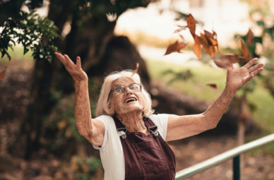 Elderly woman throwing leaves into the air smiling